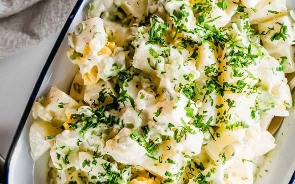 American potato salad in a bowl with green herbs.