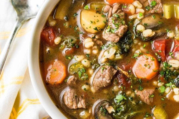 A bowl of beef and vegetable soup with a spoon.