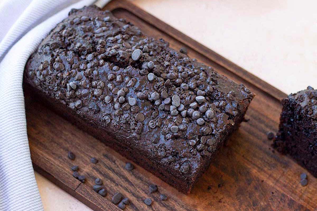 A slice of chocolate cake on a wooden cutting board.