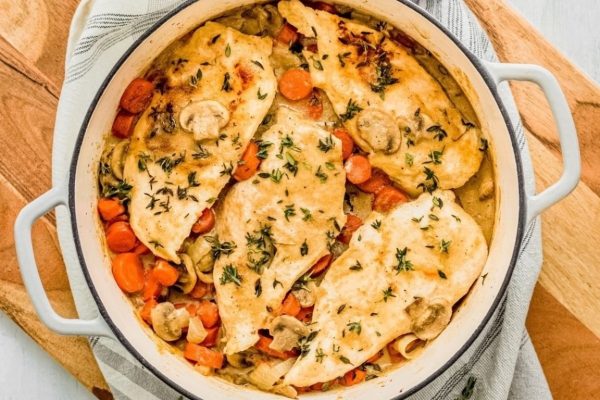 Chicken breasts in a skillet with carrots and herbs.