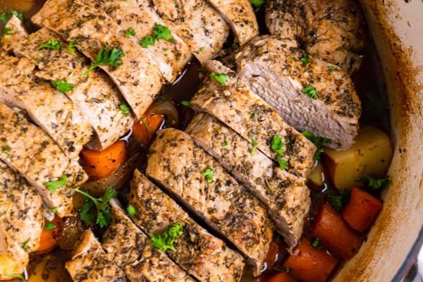 Dutch Oven Pork Tenderloin slices with vegetables and sauce.