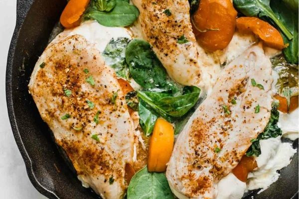 Apricot chicken breasts with greens in a black skillet.