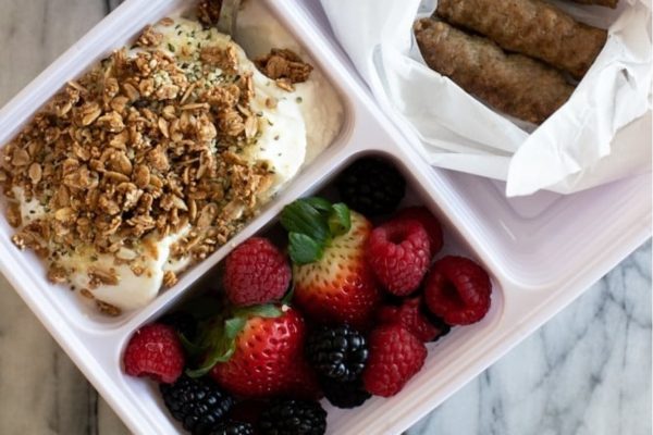 A lunch box with yogurt, granola and fruit.