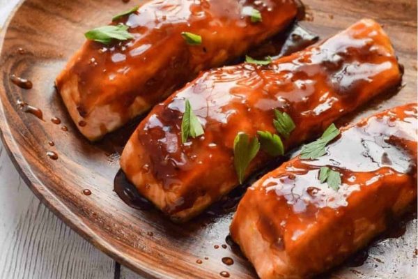 Three salmon fillets on a wooden plate.