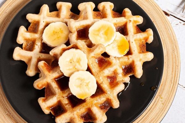 Vegan banana waffles with syrup and banana slices.