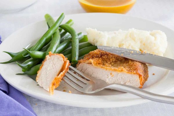 Fried pork chops with green beans on white plate.