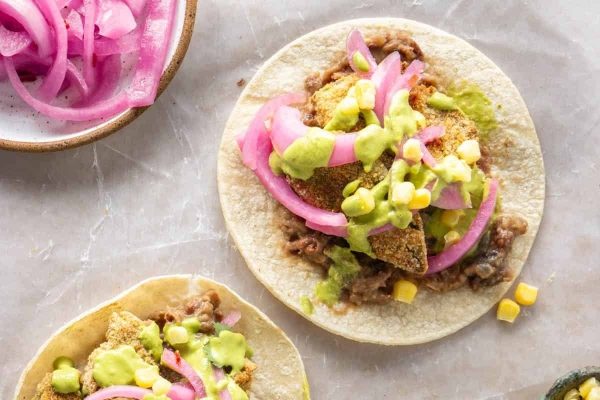 Two tacos with guacamole and red onions.