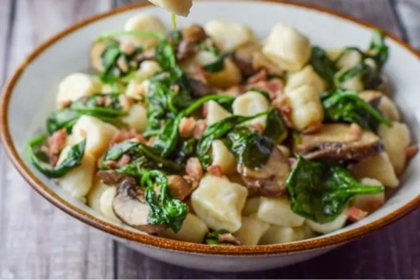 A bowl of pasta with spinach and mushrooms.