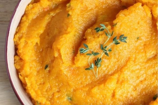 A bowl of sweet potato mashed potatoes with sprigs of thyme.