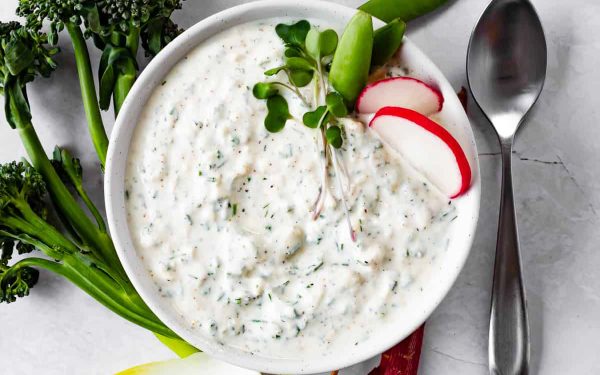 Ranch dip in a white bowl with vegetables.