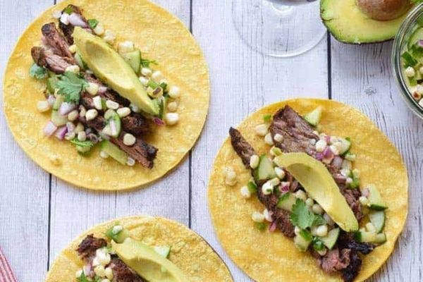 Three tacos with steak and corn salsa on a wooden table.