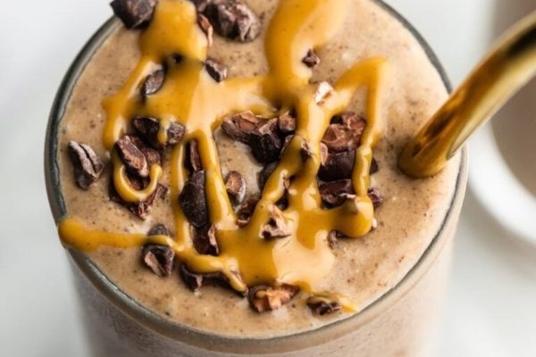Chocolate peanut butter smoothie with straw and topped with chocolate chunks and peanut butter sauce.