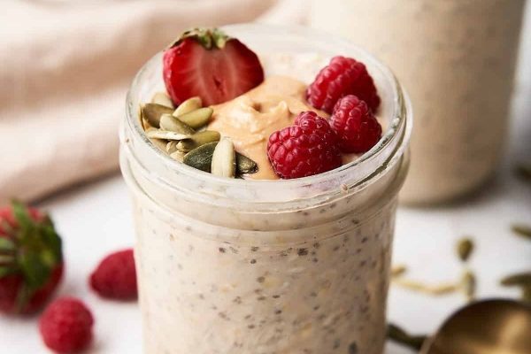 Two jars of overnight oats with raspberries and seeds.
