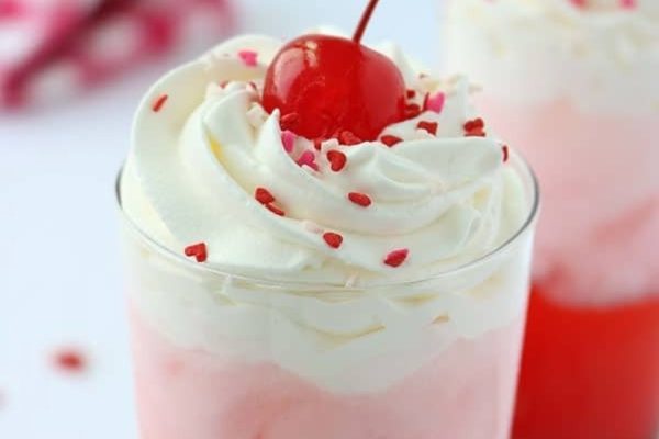 A valentine's day milkshake with whipped cream and a cherry on top.