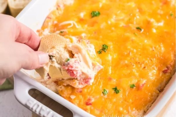 A person dipping into a dish of cheesy dip.