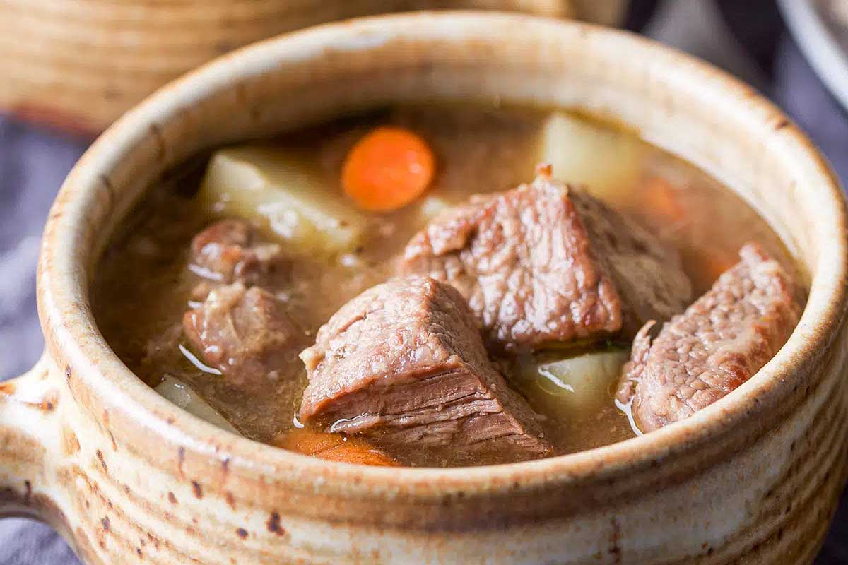 Beef stew in a mug with carrots and potatoes.