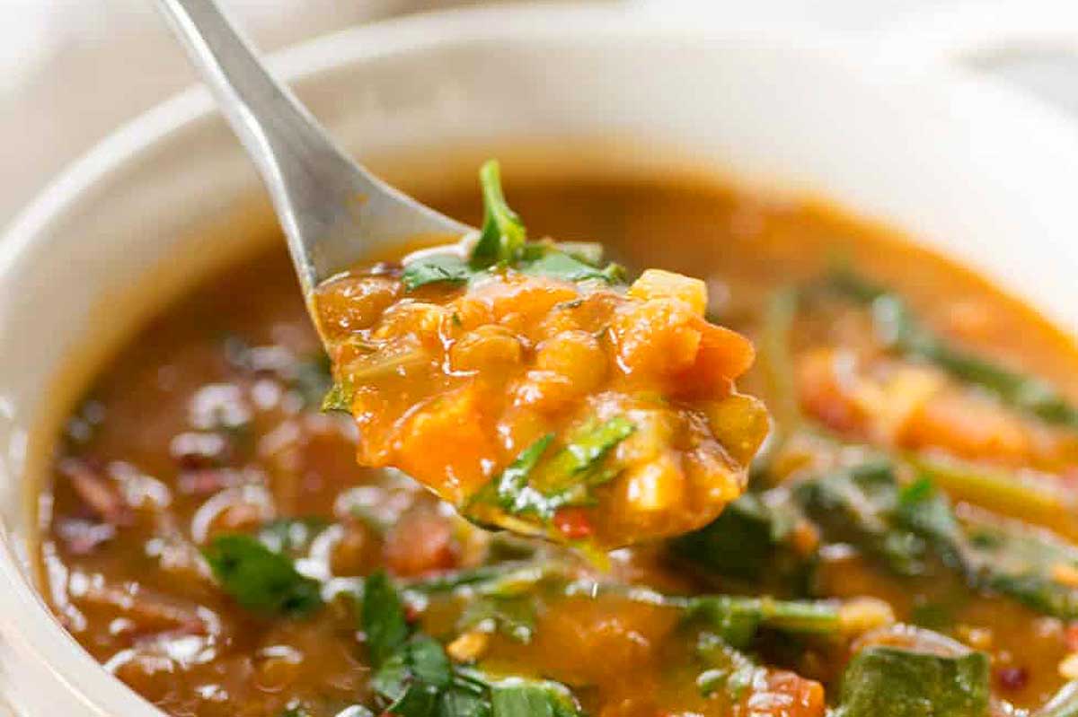 A spoonful of lentil soup in a white bowl.