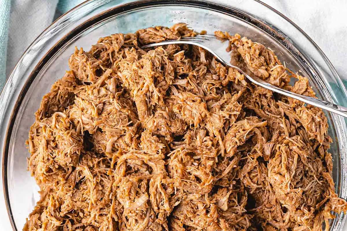 Pulled pork in a glass bowl with a fork.