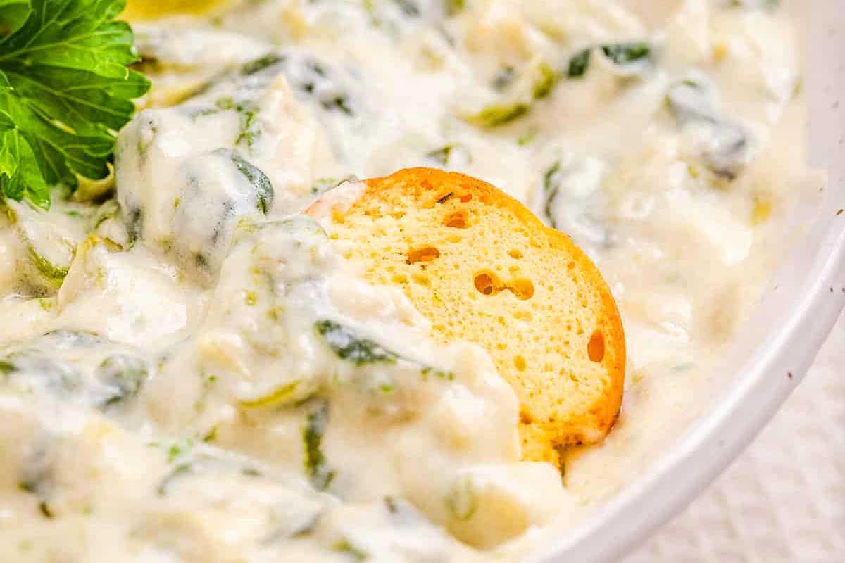 A bowl of creamy spinach dip with a slice of bread.