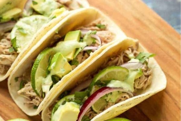 Three tacos on a wooden cutting board.