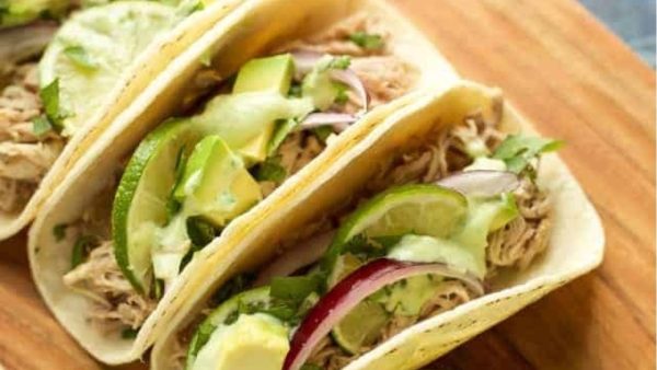 Three tacos on a wooden cutting board.