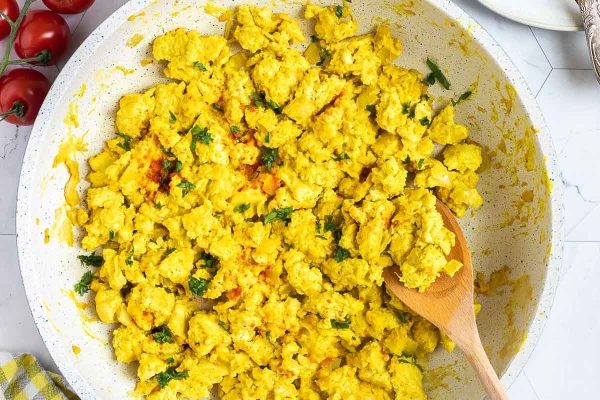 Scrambled tofu in a white bowl with a wooden spoon.