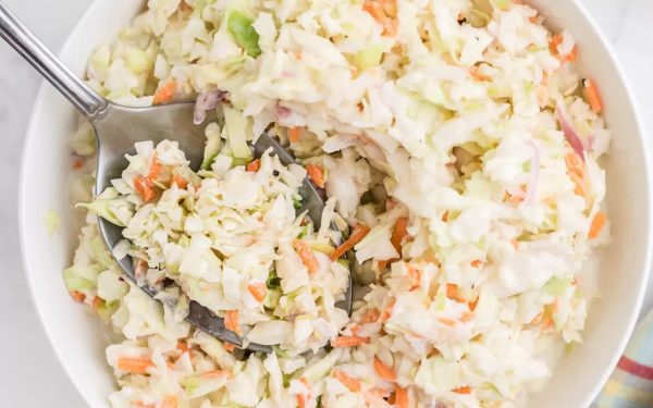 Coleslaw with a spoon in a white bowl.