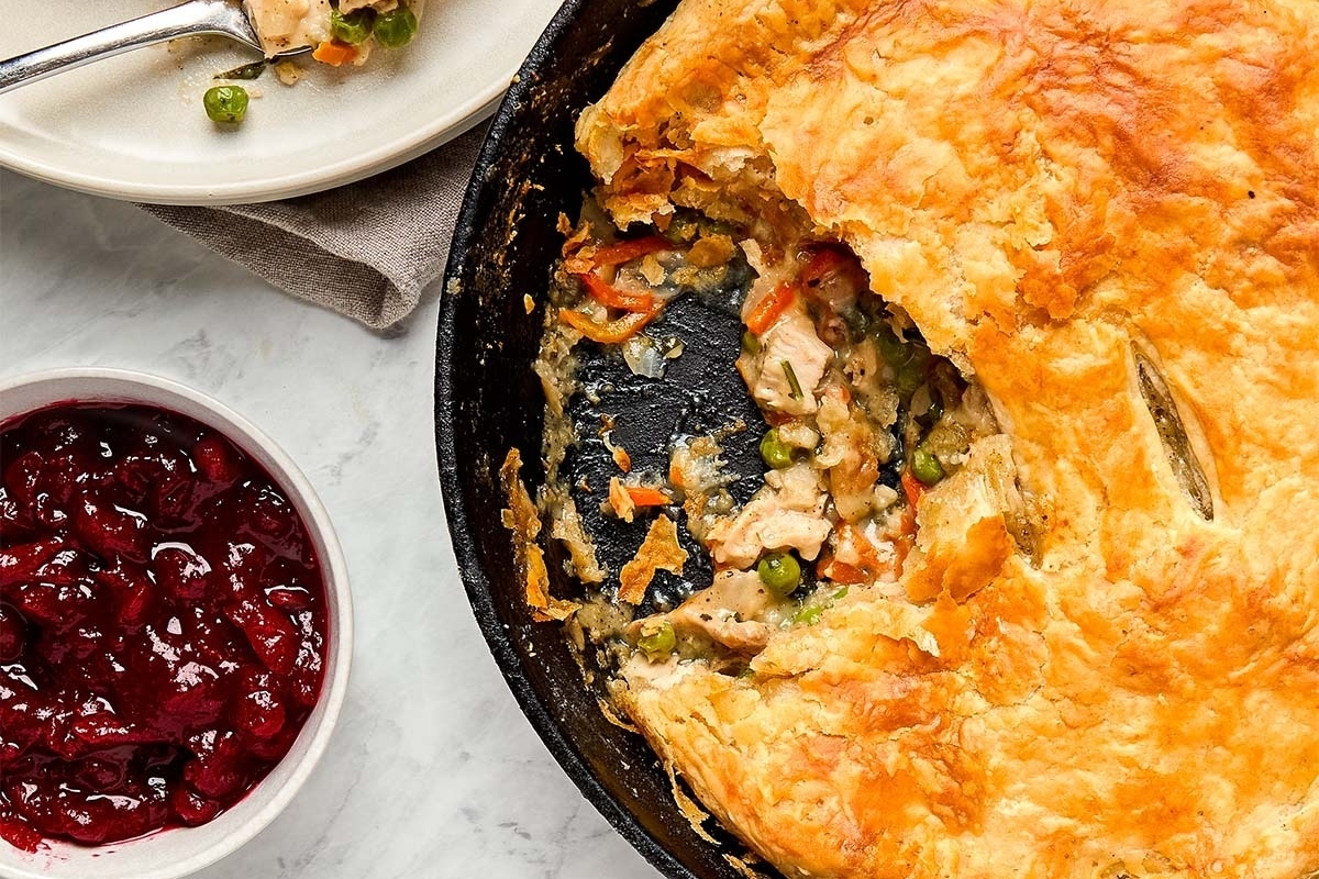 Leftover turkey pot pie in a cast iron skillet with cranberry sauce on the side. 