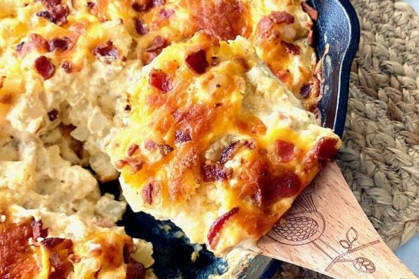 Wooden spoon scooping out Loaded Hash Brown casserole from a skillet.