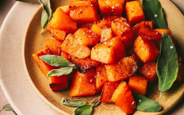 Roasted butternut squash with sage on a brown plate.