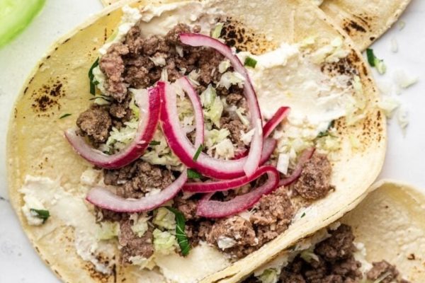 Two tacos with meat and onions on a white plate.