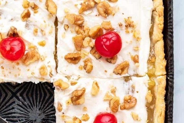 A slice of pie with cherries and nuts on top.