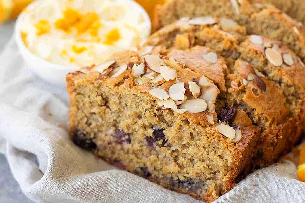 A slice of banana bread with almonds and oranges on a napkin.