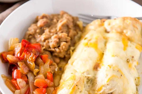 Pork enchiladas in a white bowl with beans.