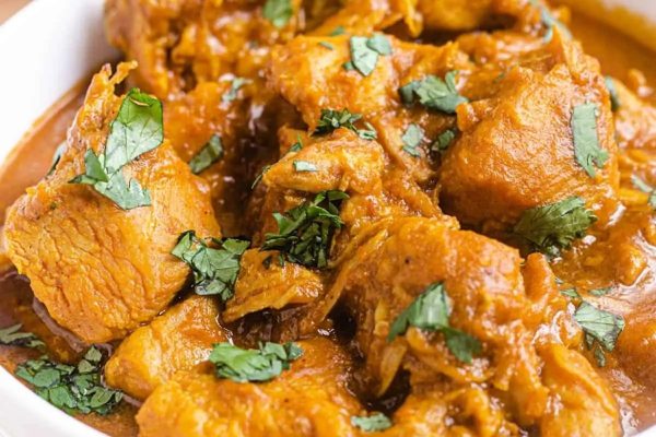 Chicken curry in a white bowl on a wooden table.