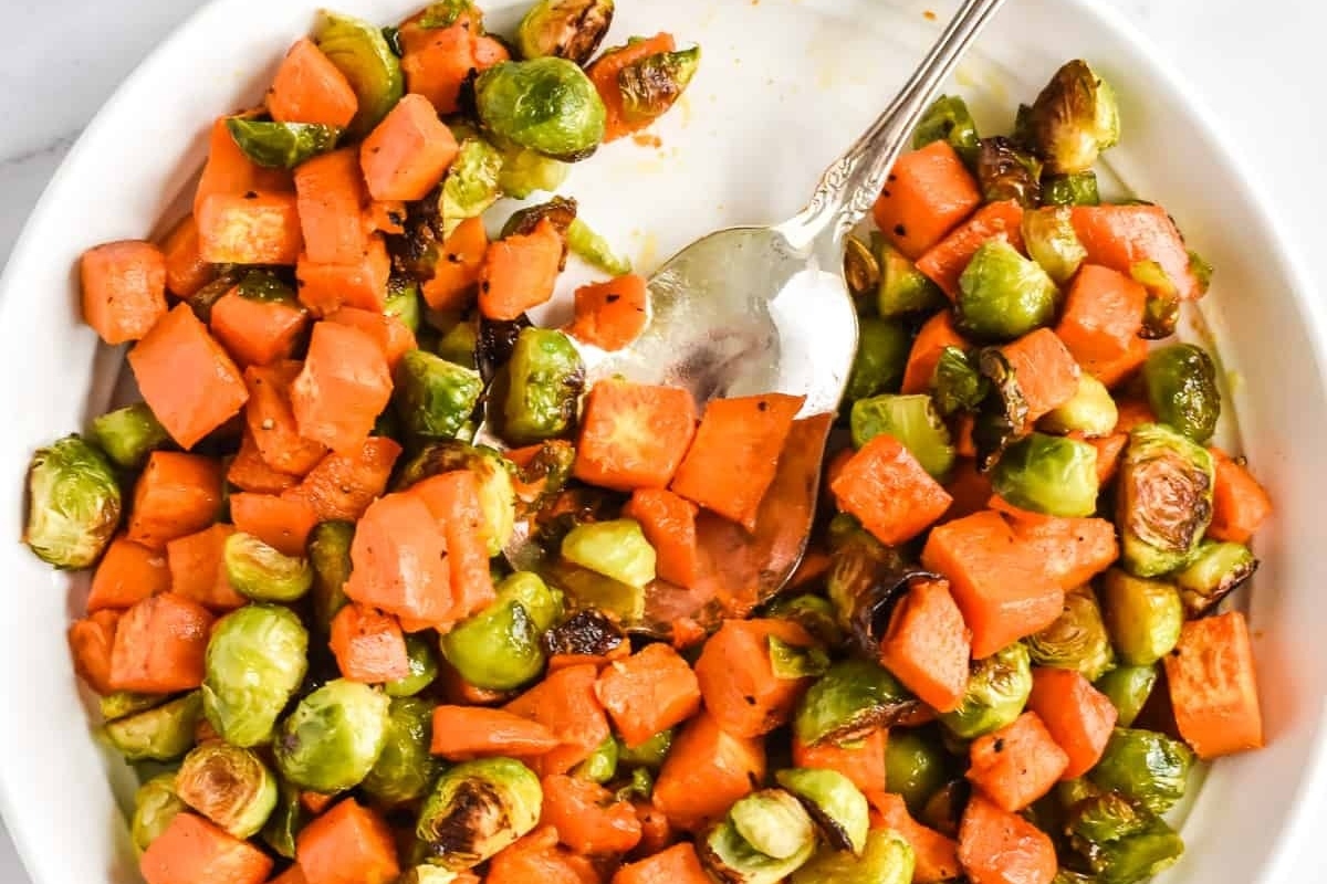 Roasted sweet potato, carrots, and brussels sprouts in a white bowl.