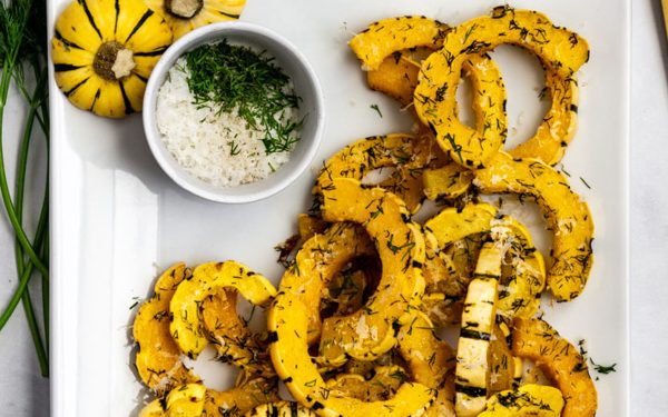 Roasted delicata squash on a white tray with herbs on side.