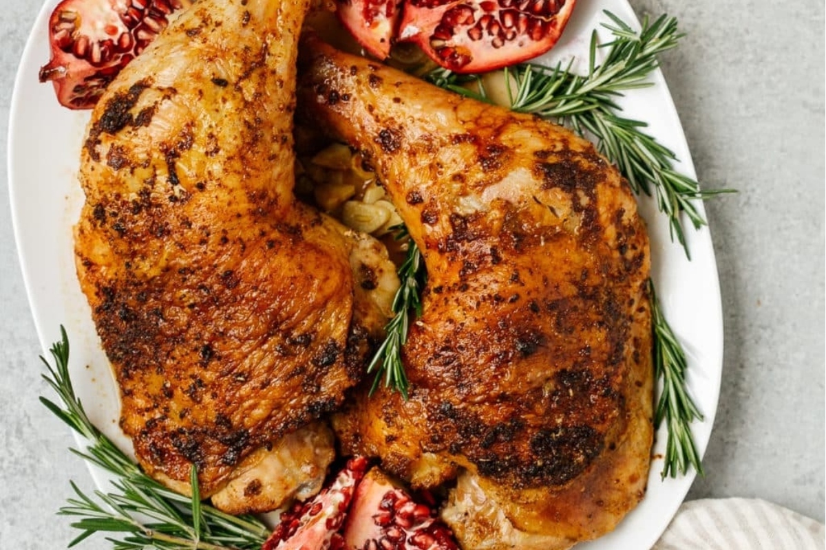 Roasted turkey legs served on a plate with pomegranate and rosemary. 