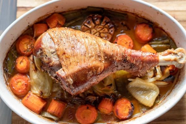 Roasted turkey leg served with gravy and vegetables on an oval dish. 
