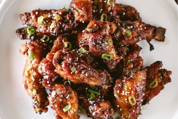Pile of sticky chicken wings on a white plate.