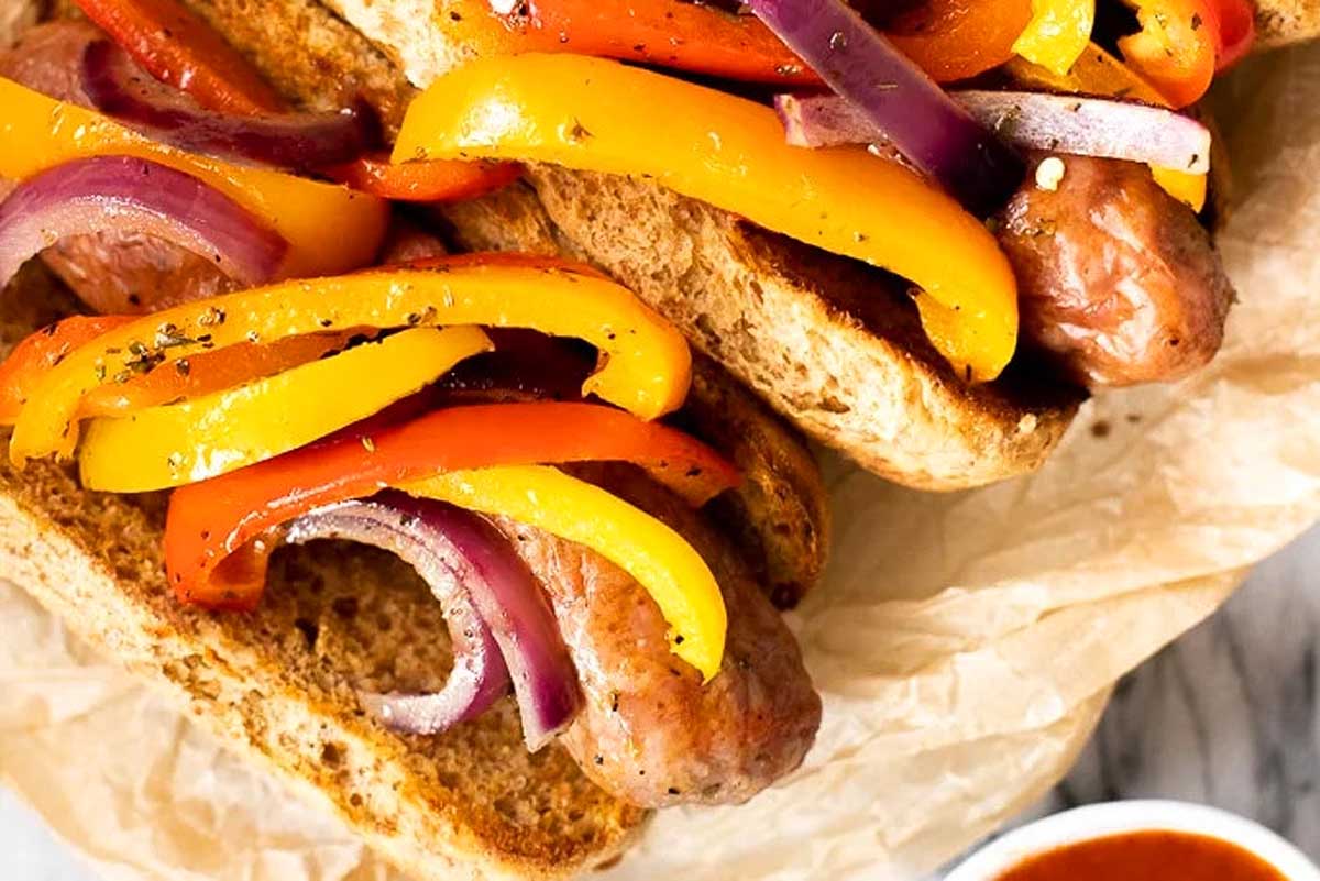 Two hot dogs with peppers and onions on a bun.