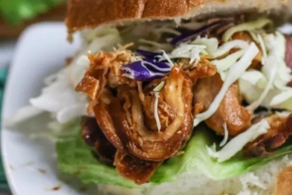 A bbq pulled pork sandwich with coleslaw on a white plate.