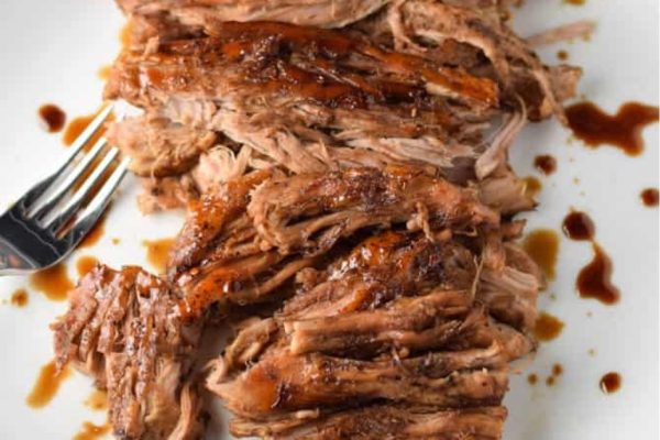 Slow cooker balsamic pork on a white plate with a fork.