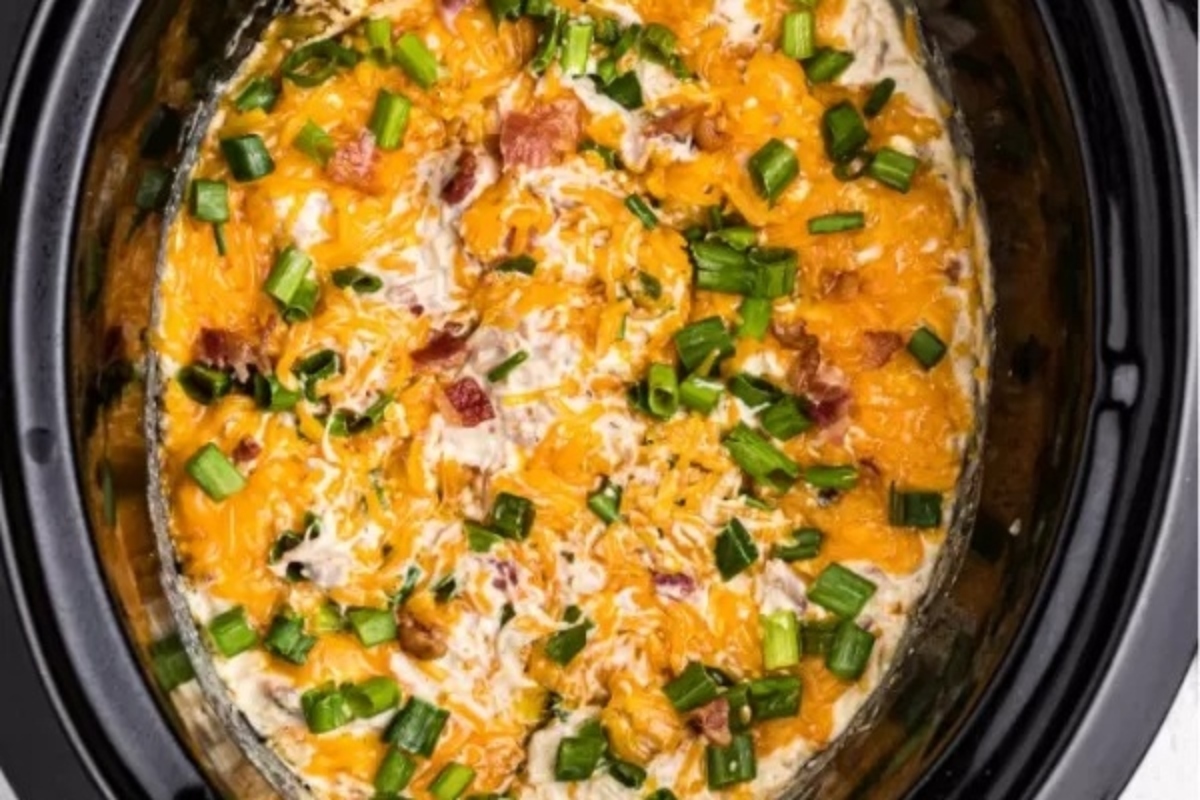 A crock pot filled with cheese and green onions.