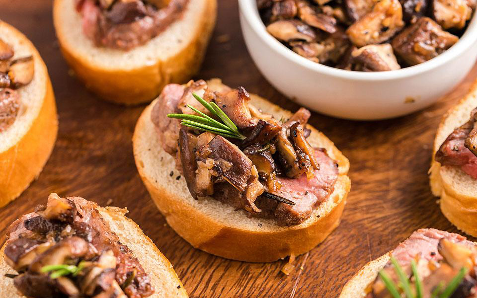 Steak and mushrooms on toast on a brown board.