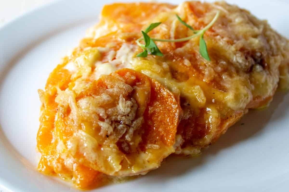 A tantalizing plate of sweet potato casserole with a sprig of thyme, showcasing one of the best sweet potato recipes around.
