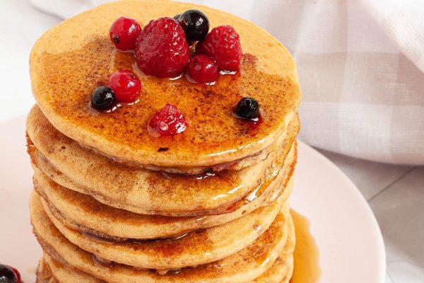 A stack of pancakes with berries and syrup.