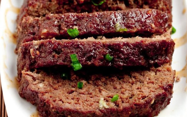 Sliced meatloaf on a white plate with sauce.