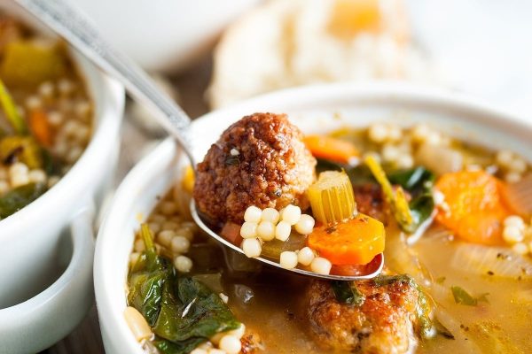 Italian wedding soup scooped out in a spoon from a bowl.