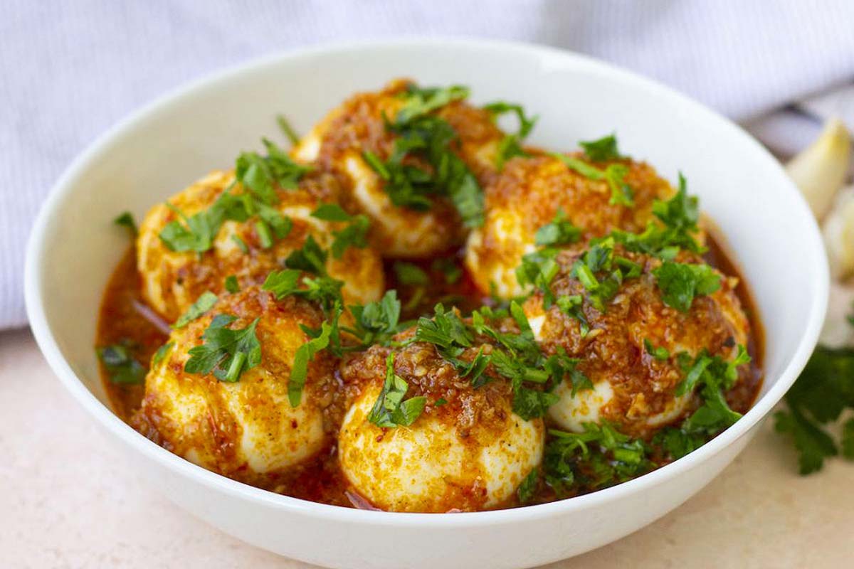 Boiled eggs in a bowl with sauce and fresh herbs.